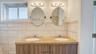 Double vanity featuring a stone countertop, dual undermount sinks, wood-finish cabinetry, two oval mirrors, and horizontal tile wall surrounds