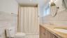 Dual-sink vanity with stone-surfaced countertop, wood-finish cabinetry, ceramic tile wall cladding, and walk-in shower enclosure