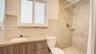 Bathroom featuring stone-tile wall surround, wood-finish vanity cabinetry, stone-slab countertop with integrated oval sink, and a handheld shower fixt