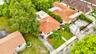 Aerial perspective of a property featuring a clay tile roof, concrete driveway, manicured lawn, and mature landscaping