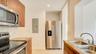 Kitchen featuring flat-panel wood-finish cabinetry, stainless steel appliances, stone countertops, textured stone tile backsplash, and a double-basin 