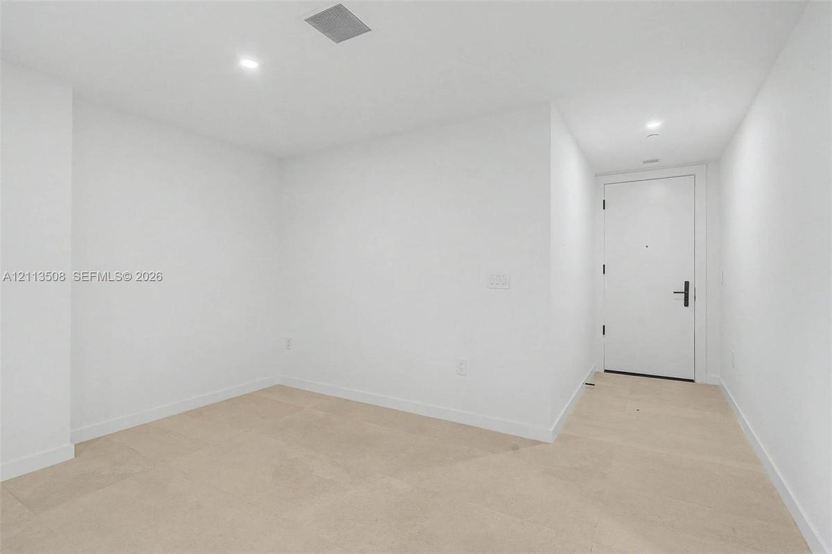 Neutral interior featuring light-toned flooring, recessed lighting, and a solid-core door with matte black hardware