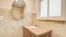 Stone-tiled walls, vanity with stone countertop and integrated sink, oval wall-mounted mirror, and frosted glass window
