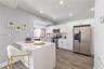 Kitchen featuring white shaker-style cabinetry, quartz countertops with waterfall edge, stainless steel appliances, recessed lighting, and wood-finish
