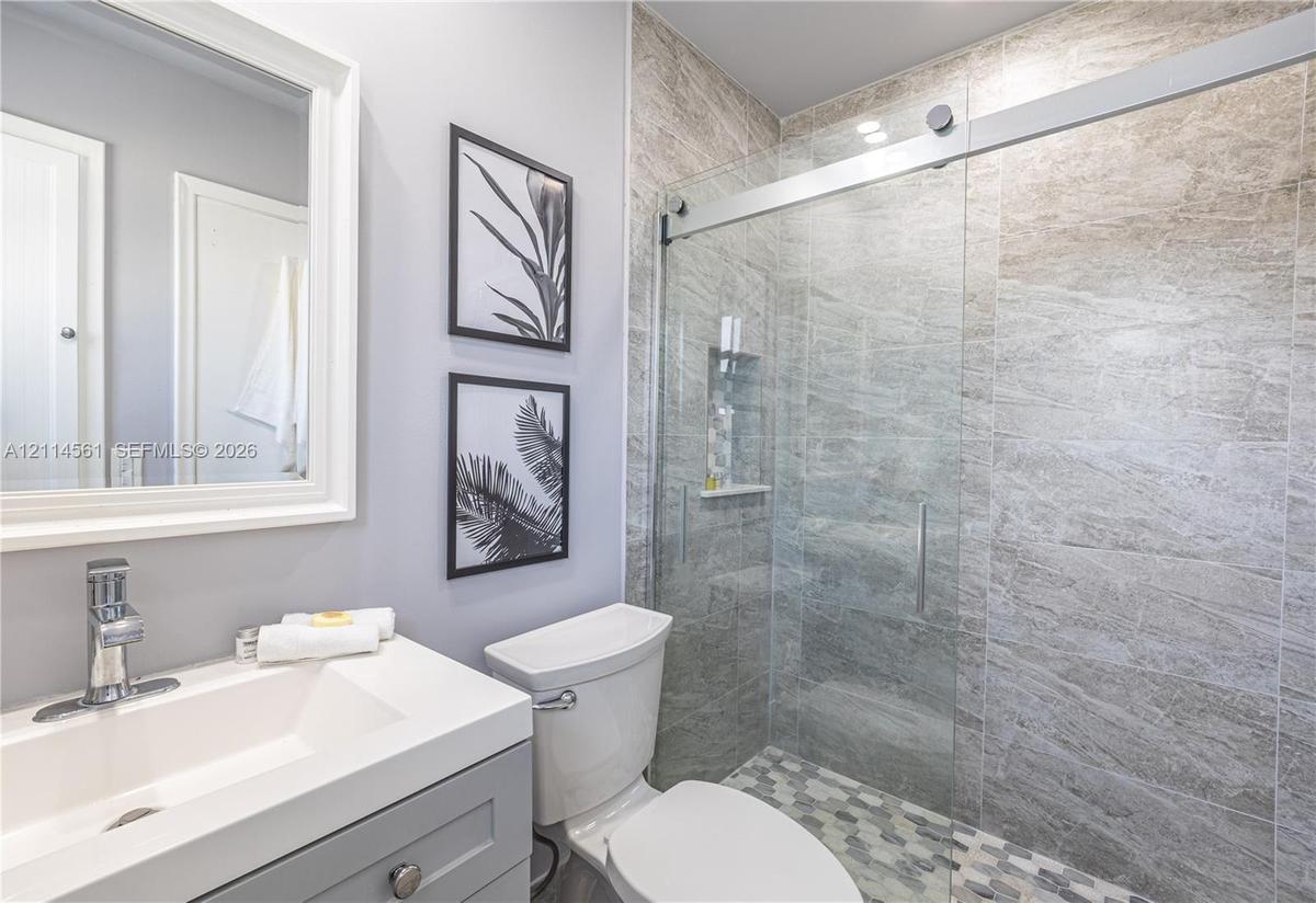 Bathroom featuring a vanity with a white countertop and chrome faucet, a walk-in shower with stone-tile surround, glass sliding door, and hexagonal fl