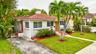 Single-story exterior featuring white stucco siding, a tiled hip roof, a concrete driveway, and mature palm landscaping