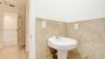 White pedestal sink featuring a dual-handle chrome faucet, complemented by neutral-toned tile wainscoting and light wood-finish flooring