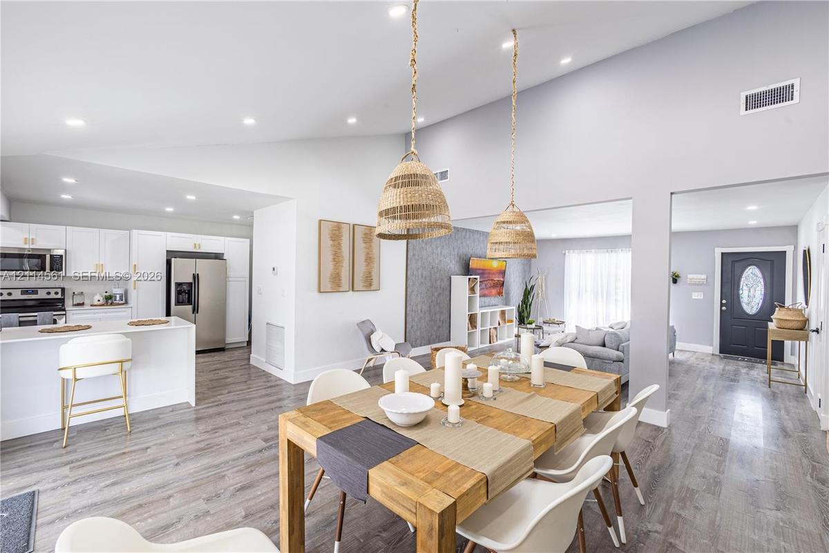 Vaulted ceilings, open-concept kitchen with white cabinetry and stainless steel appliances, wood-finish flooring, and natural-textured pendant lightin