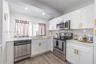 Kitchen featuring white shaker-style cabinetry, metallic gold hardware, stainless steel appliances, light-toned stone-finish countertops, and wood-fin