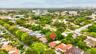 Aerial view featuring a residential property with a multi-level tile roof, surrounding mature landscaping, and an established street grid
