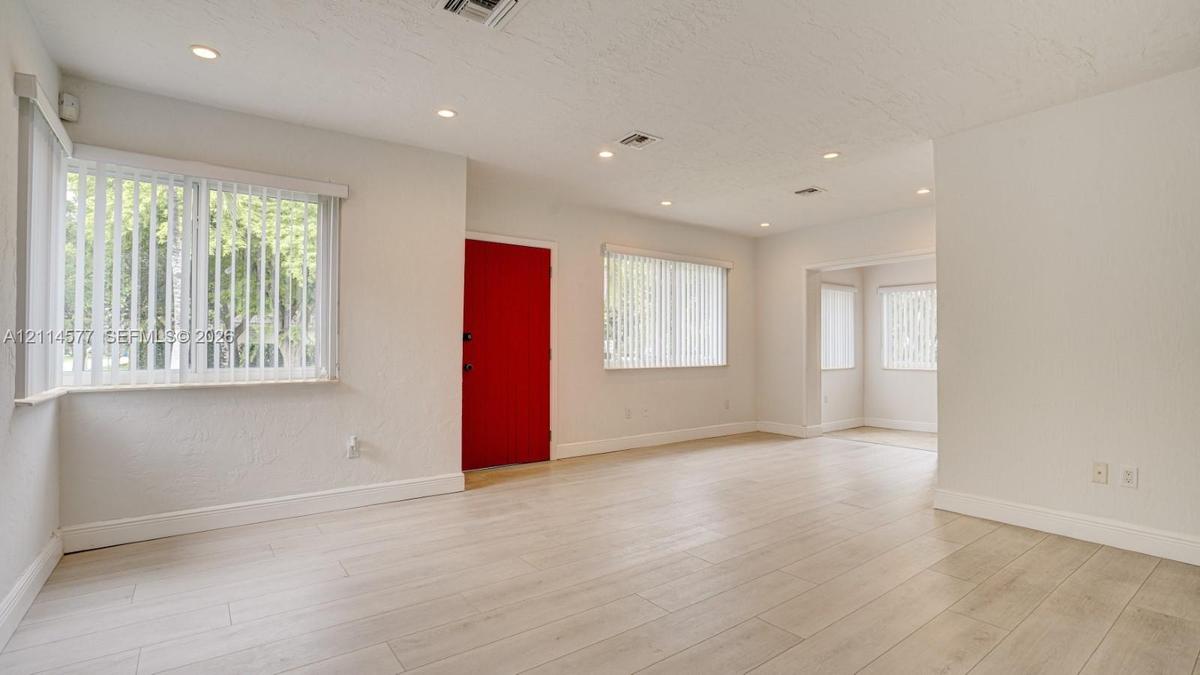 Neutral interior featuring wood-finish flooring, recessed lighting, multiple windows with vertical blinds, and a solid red-finish front door