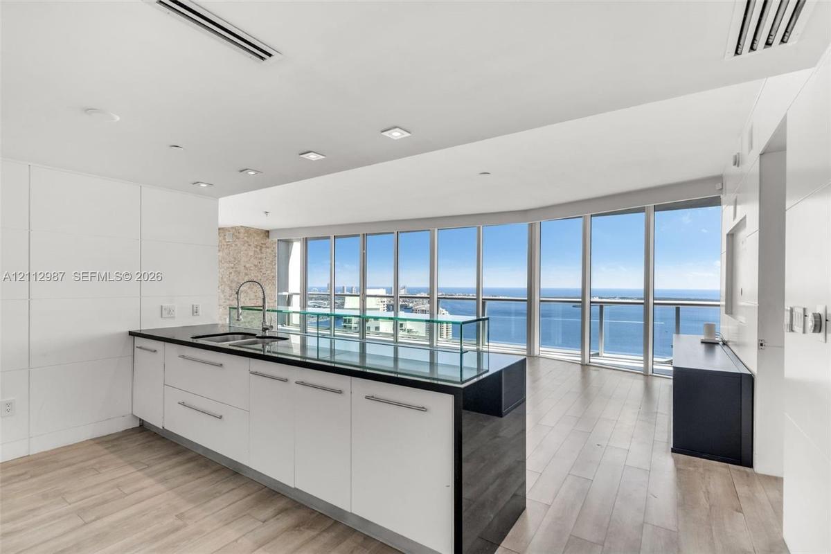 Kitchen featuring a central island with a dark stone countertop, integrated glass backsplash, white cabinetry with metal hardware, floor-to-ceiling wi