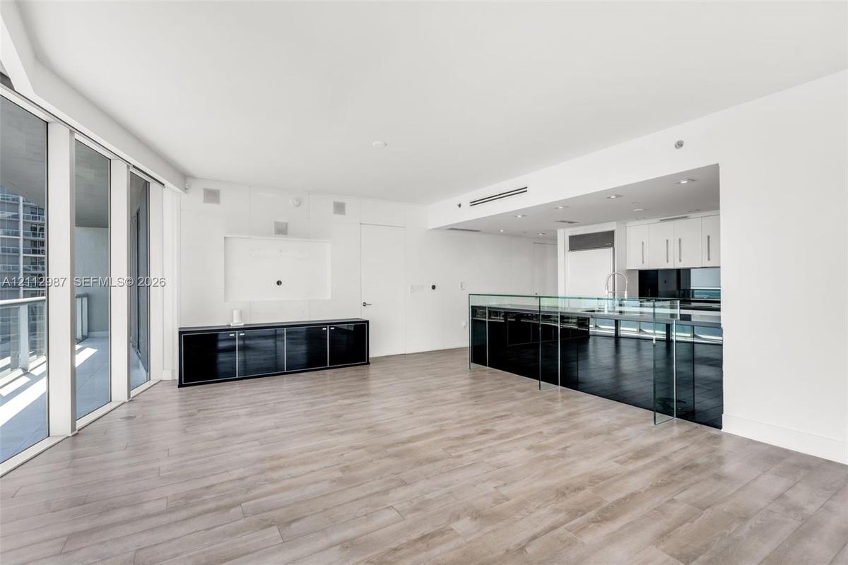 Open-concept floor plan featuring wood-finish flooring, floor-to-ceiling glass wall, built-in black lacquer cabinetry, and a kitchen island with a gla