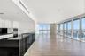 Open-concept interior featuring floor-to-ceiling windows, wood-finish flooring, a kitchen with black countertops and white cabinetry, and a stone-clad