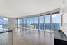 Floor-to-ceiling windows, wood-finish flooring, stone-veneer accent pillar, glass-panel balcony railing, and expansive water backdrop