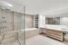 Floating wood-finish vanity with dual vessel sinks, glass-enclosed shower, built-in soaking tub, textured stone accent wall, and expansive frameless v