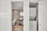Stacked laundry unit set within a custom closet, featuring a floating vanity with a vessel sink, textured stone-tiled wall, and wood-finish flooring