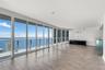 Floor-to-ceiling glass windows, wide-plank wood-finish flooring, and glass-railing balcony featuring expansive water and city skyline panoramas