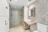 Bathroom featuring a pebble-tiled accent wall, floating wood-finish vanity with a white vessel sink, and a walk-in glass-enclosed shower with polished