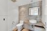 Textured stone accent wall featuring a wall-mounted wood-finish vanity, circular vessel sink, single-lever faucet, and wood-finish flooring
