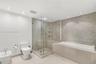 Bathroom featuring a frameless glass shower enclosure, a soaking tub with stone-tiled surround, a textured stone accent wall, recessed lighting, and a