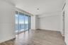 Floor-to-ceiling windows, wood-finish flooring, balcony with glass railing, and water backdrop
