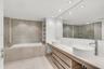Bathroom featuring dual vessel sinks, a custom vanity with wood-finish cabinetry, a textured stone accent wall, a soaking tub, and a frameless glass s