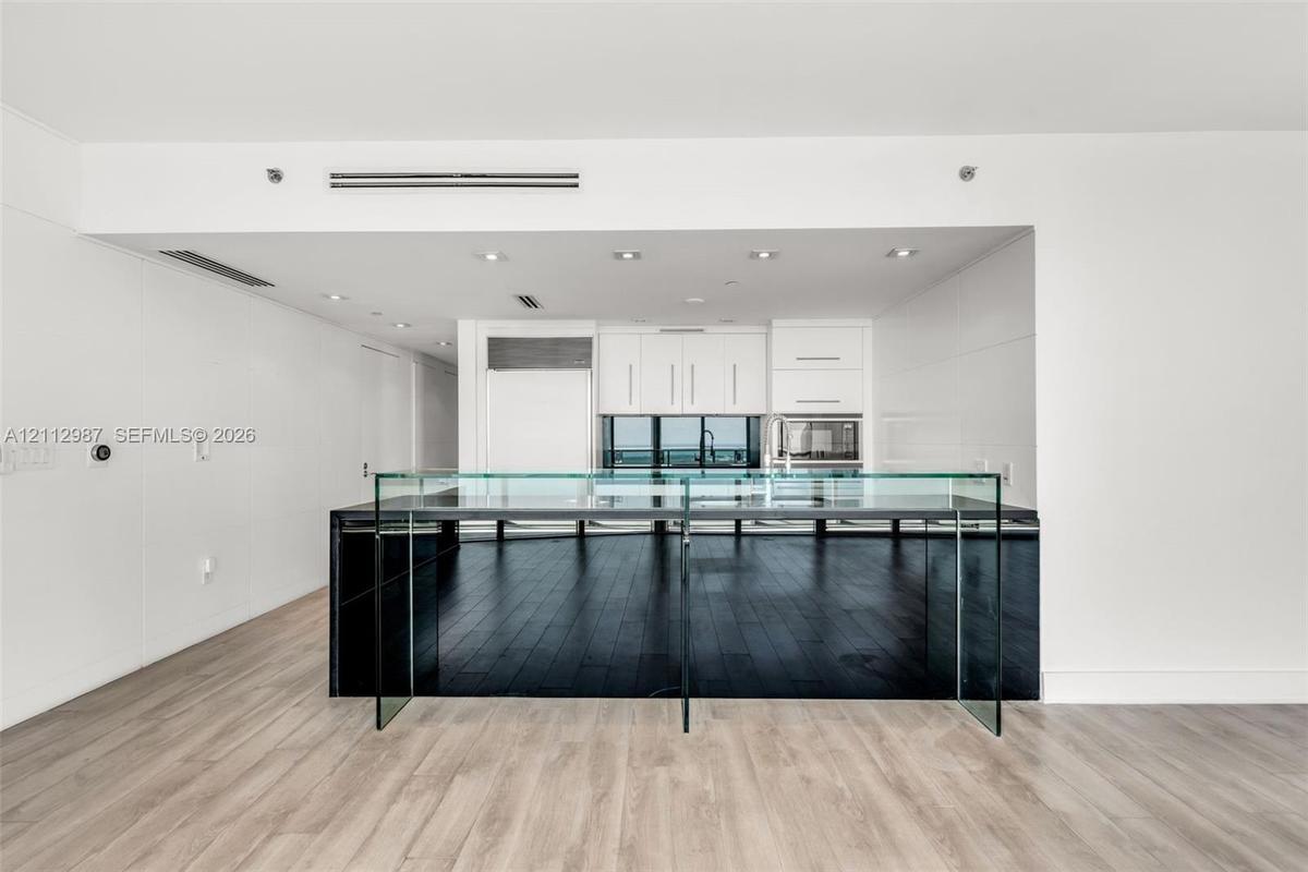 Kitchen featuring custom white cabinetry, integrated refrigerator, built-in microwave, minimalist glass-paneled island, and wood-finish flooring