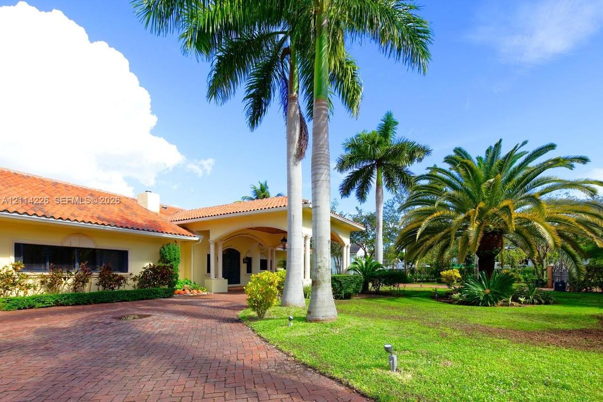 Exterior featuring a terracotta tile roof, brick paver driveway, covered entryway with classical columns, and mature palm trees
