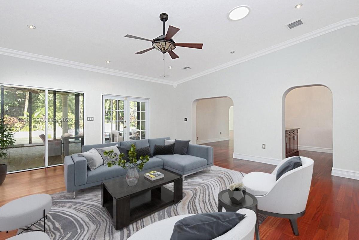 Living area featuring wood-finish flooring, vaulted ceilings with crown molding, a central ceiling fan, recessed lighting, and a tubular skylight, com