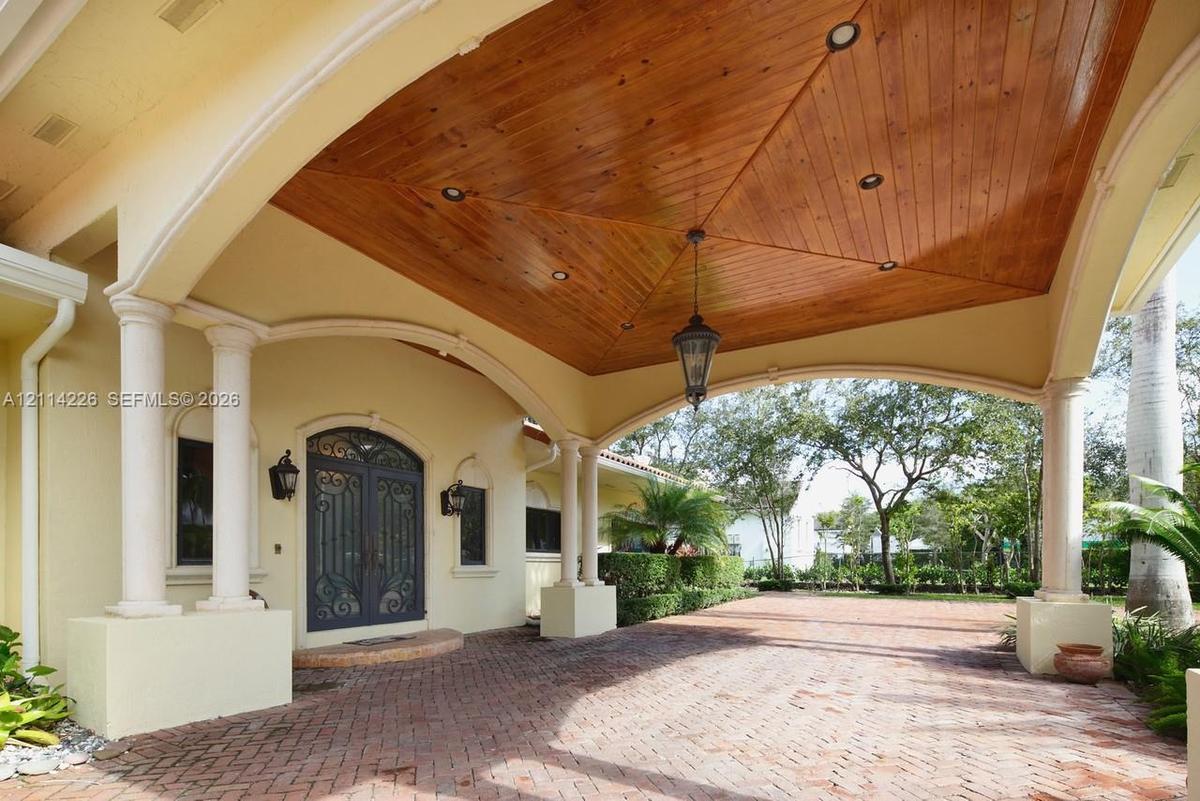 Covered porte-cochère featuring a wood-plank vaulted ceiling, recessed lighting, ornate double front entry doors, and brick paver flooring supported b