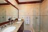 Bathroom featuring a granite countertop vanity with dual undermount sinks, custom dark wood cabinetry, a glass-enclosed shower with tiled walls, and c