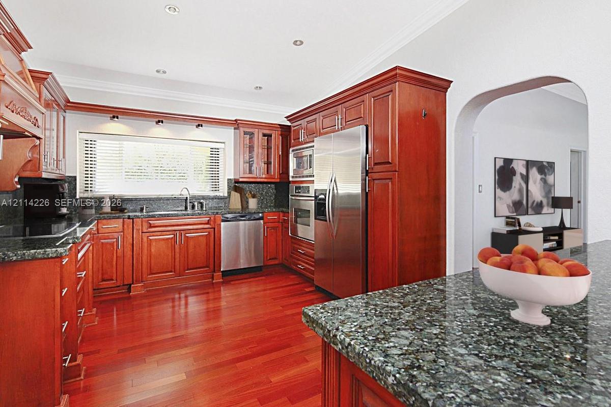 Kitchen featuring rich wood cabinetry, stone countertops, stainless steel appliances, recessed lighting, and wood-finish flooring