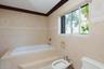 Built-in soaking tub with a tiled surround, neutral ceramic wall tile, dark wood crown molding, sliding window, and a porcelain bidet