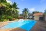 In-ground swimming pool with built-in water feature and tiled steps, surrounded by stone-paver decking and mature tropical landscaping