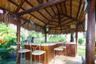 Outdoor palapa featuring a thatched roof, exposed timber support beams, and a built-in bar with wood-panel base and brick-trim countertop