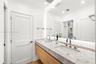 Floating vanity with wood-finish cabinetry, stone countertop, integrated dual undermount sinks, tall arch-neck faucets, and large wall-to-wall mirror 