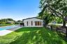 Exterior rear elevation featuring white stucco siding, a rectangular swimming pool with paved surround, expansive manicured lawn, and black metal peri