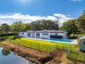 Single-story residence featuring a white exterior, expansive concrete patio, inground swimming pool, and water frontage