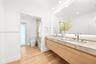 Floating dual vanity with stone countertop, under-mount sinks, modern metal faucets, wood-finish cabinetry, and oversized wall-mounted LED mirror