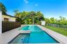 Swimming pool with an integrated sun shelf, mosaic tile waterline, concrete pool deck, dark wood-finish privacy fencing, and a detached storage shed