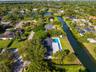 Aerial perspective of a waterfront property featuring a swimming pool, expansive lawn, mature tree canopy, and canal frontage