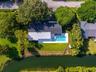 Aerial perspective featuring a waterfront property with an in-ground swimming pool, concrete pool deck, expansive lawn, and mature landscaping