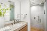 Bathroom featuring a stone-surface vanity with an integrated sink, wood-finish cabinetry, a large wall-mounted mirror, and a walk-in glass-enclosed sh