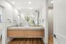 Floating vanity featuring wood-finish cabinetry, dual undermount sinks, stone countertop, and full-width wall mirror