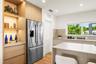 Kitchen featuring flat-panel cabinetry, light-toned stone-finish countertops, stainless steel refrigerator, integrated wood-finish shelving with reces