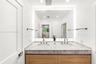 Dual-sink vanity featuring stone-finish countertop, wood-finish cabinetry, under-mount sinks, and wall-to-wall integrated backlighting