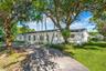 Single-story residence featuring a white painted exterior, asphalt driveway, mature canopy trees, and established landscaping