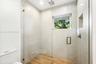 Walk-in shower featuring a glass enclosure, wood-finish tile flooring, ceiling-mounted rainfall showerhead, recessed wall niche, and large-format tile