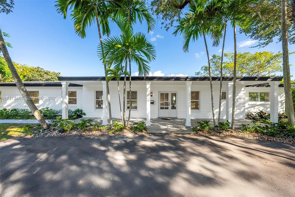 Single-story exterior featuring white horizontal siding, a covered entryway with square columns, double glass-paneled front doors, and established pal